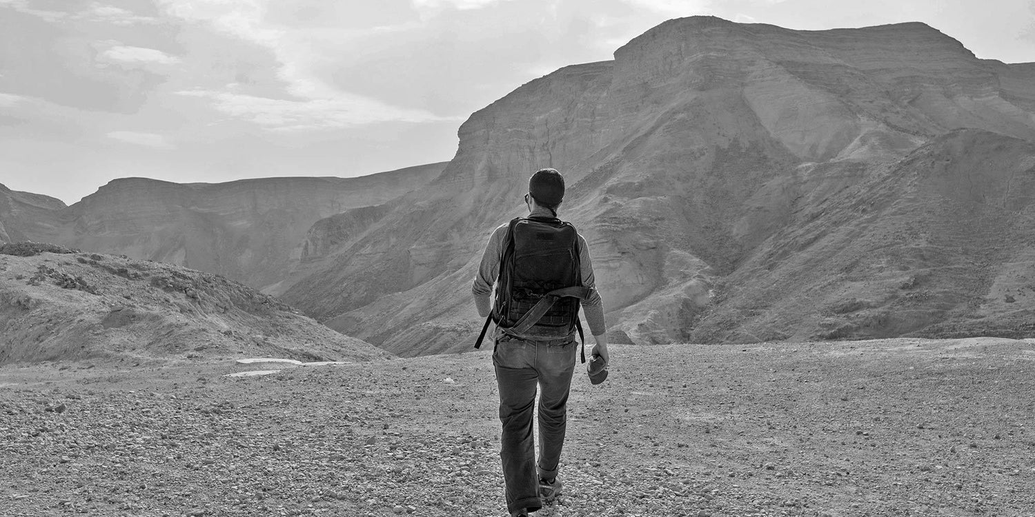 Person rucking with a GORUCK backpack in a rugged mountain landscape, adventure gear