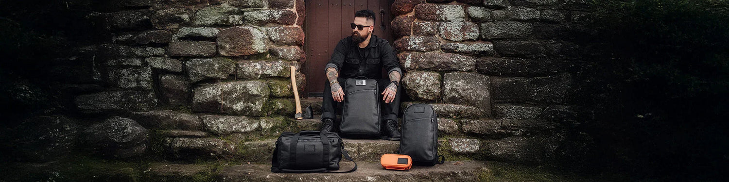 Man sitting on stone steps with GORUCK rucksacks and gear in rugged outdoor setting