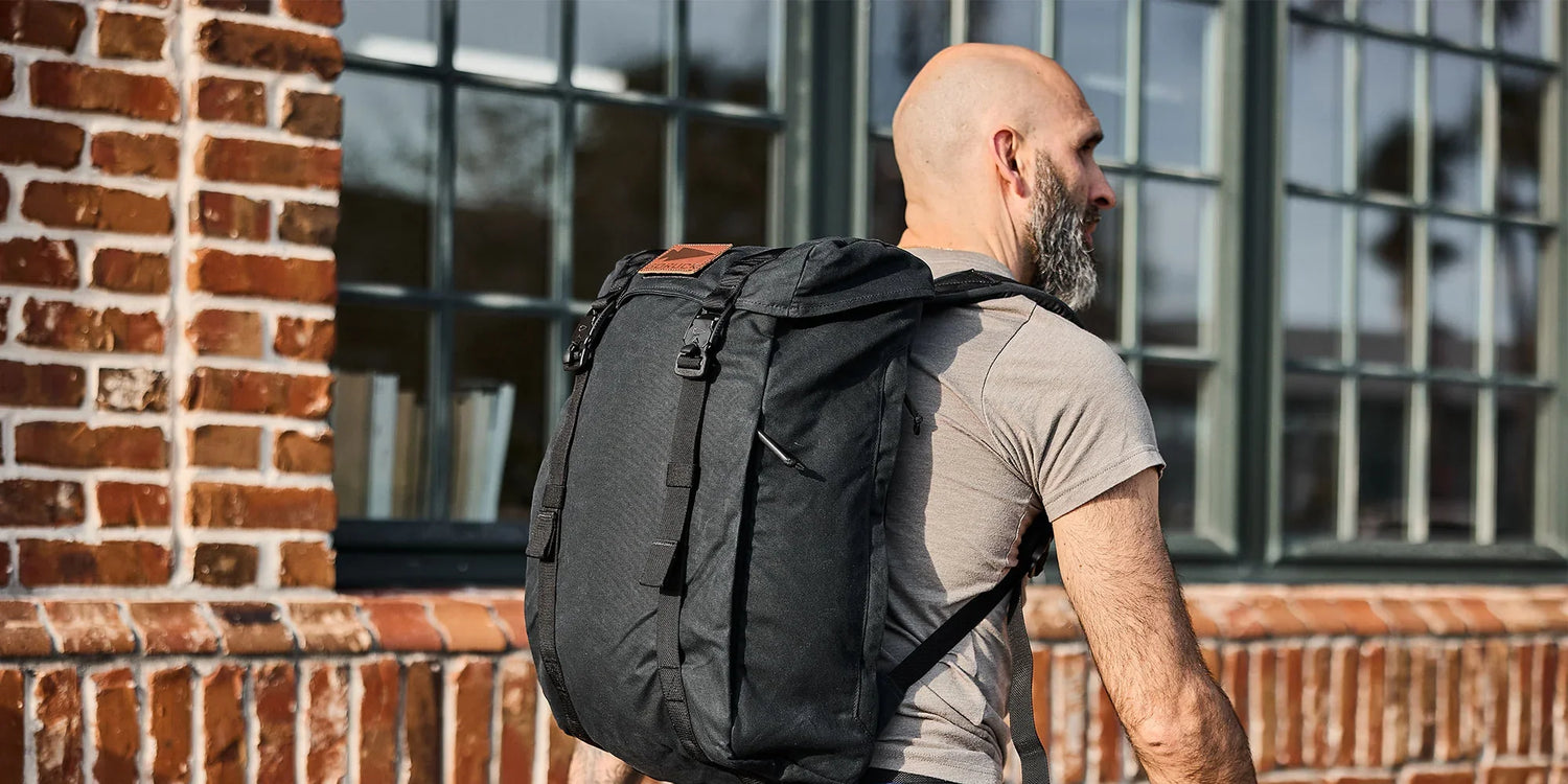 Man wearing GORUCK black rucksack outdoors by brick building, showcasing rucking gear