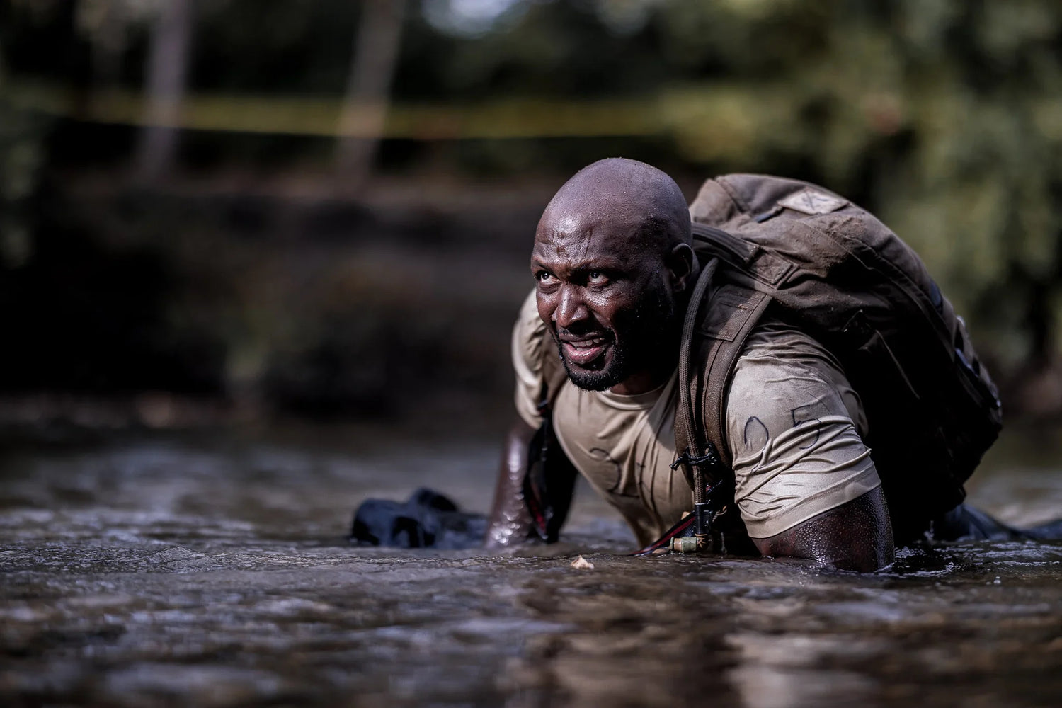 Man wearing GORUCK rucksack crawling through muddy water during outdoor rucking event