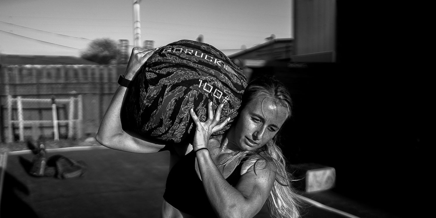 Athletic woman lifting a 100lb GORUCK sandbag in outdoor training setting