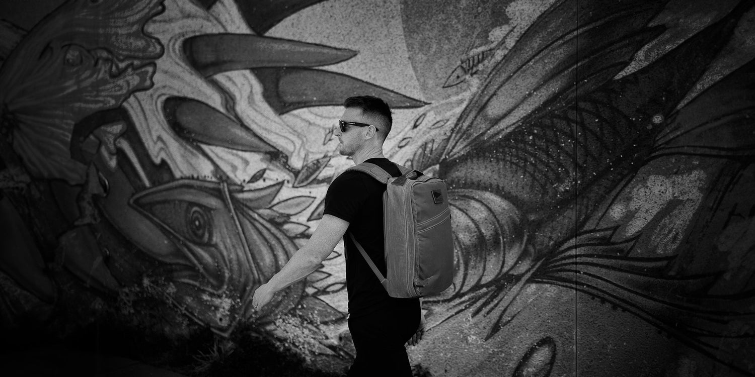 Man wearing GORUCK backpack walking past detailed fish mural on urban wall