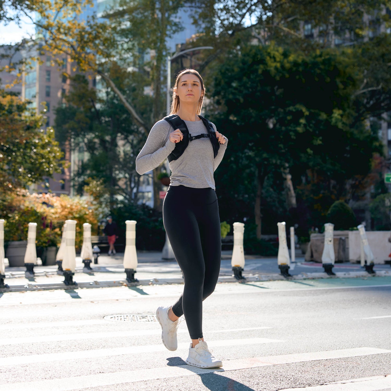 A woman wearing the Spy Ruck | Women's Weighted Vest walks across a city street crosswalk on a sunny day.