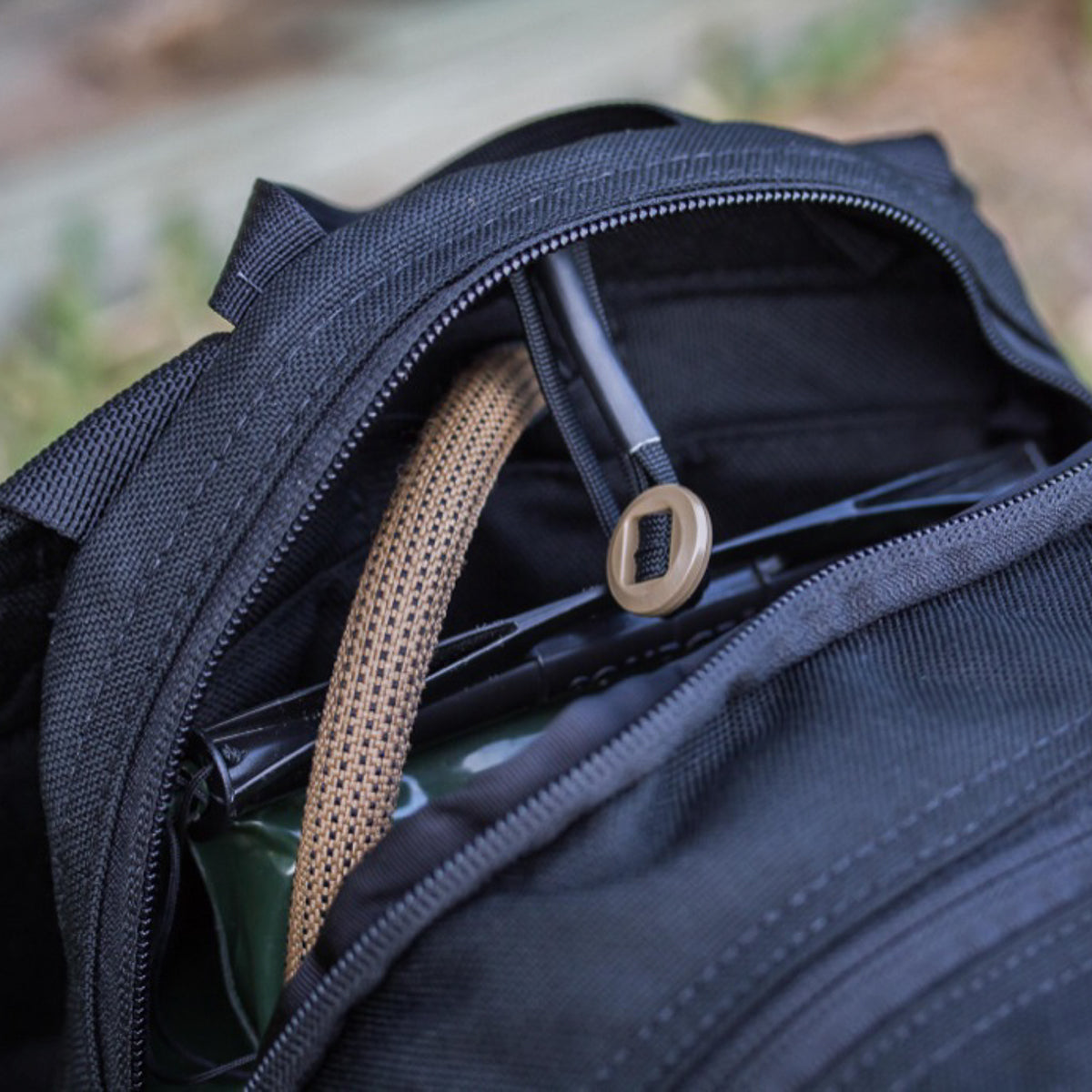Close-up of the Bullet Ruck USA Throwback, a black daypack made with durable CORDURA, shown partially unzipped to reveal a hydration tube and hose inside.