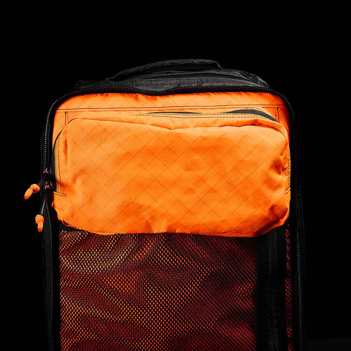The GR2 USA x Carryology - Ultra Black is an orange and black backpack made with Challenge Sailcloth UHMWPE fabric and features a zippered front pocket, shown against a black background.