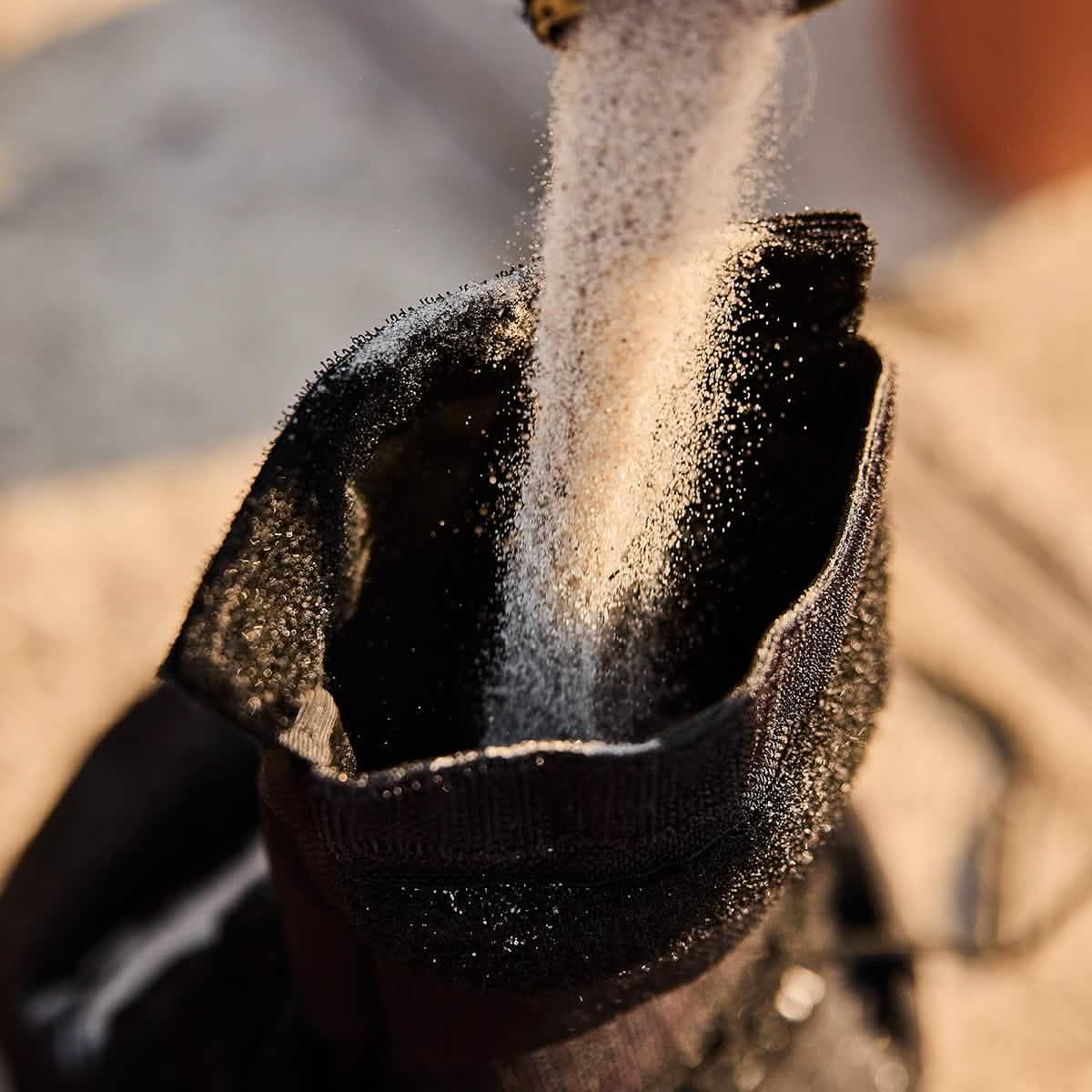 Close-up of sand pouring into a black GORUCK ruck sack on a sunlit surface