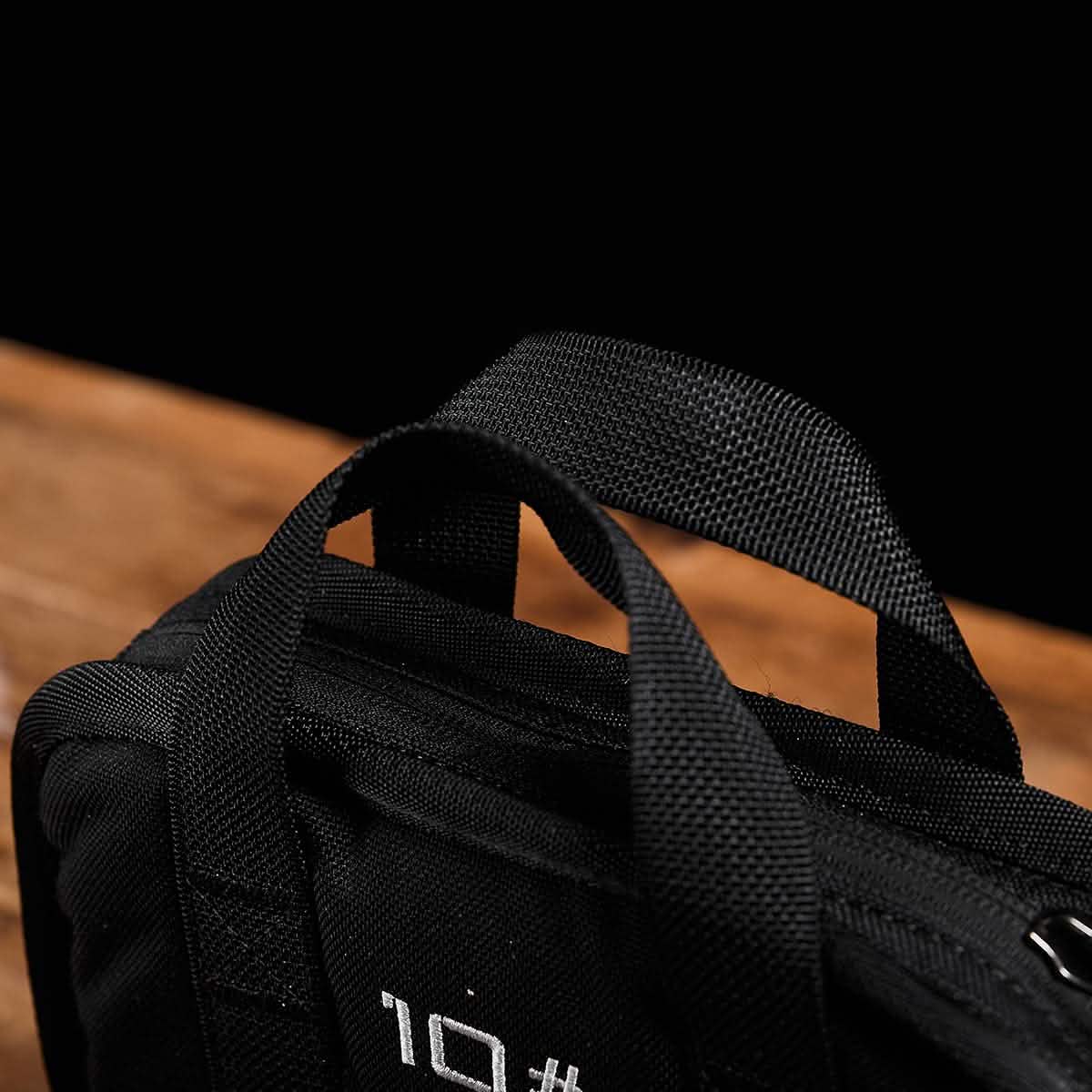 Close-up of a black backpack handle, positioned against a dark background. The sturdy handle suggests the durability inherent in the GORUCK design, with part of the Sand Ruck Plates visible and hinting at white text promising a lifetime guarantee.