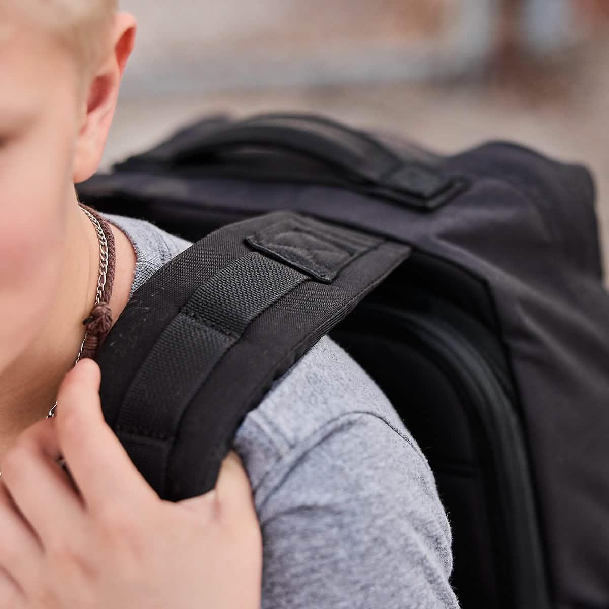 Close-up of person wearing gray shirt and black GORUCK rucksack with padded shoulder straps