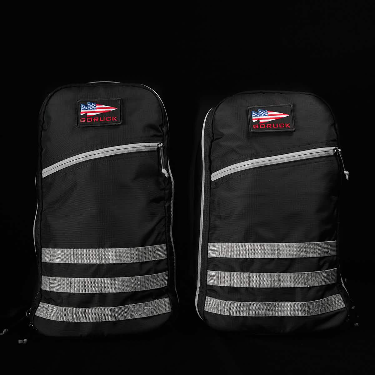 Displayed against a dark background, two identical GORUCK Bullet Ruck Laptop backpacks, crafted from durable 16L Ripstop ROBIC® Nylon with gray straps and zippers, stand out. Each backpack features a USA flag patch alongside the GORUCK label. With their rugged, minimalist design, they offer lumbar support and a laptop compartment for maximum utility.