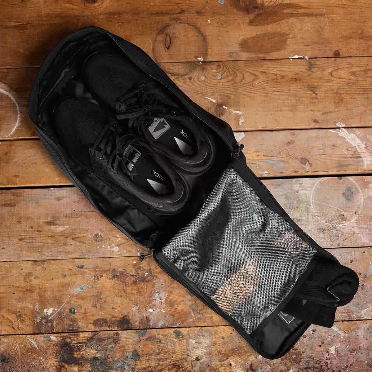 GORUCK gym bag with black athletic shoes and mesh pocket on rustic wooden floor