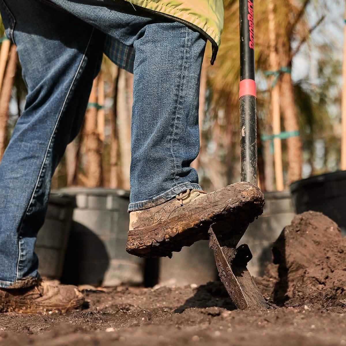 Person in rugged boots and jeans digging soil with a shovel, GORUCK outdoor gear in action