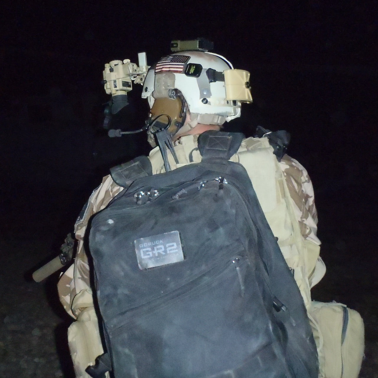 A soldier wearing a helmet and carrying a GR2 USA - Cordura rucksack stands outside at night, facing away from the camera.