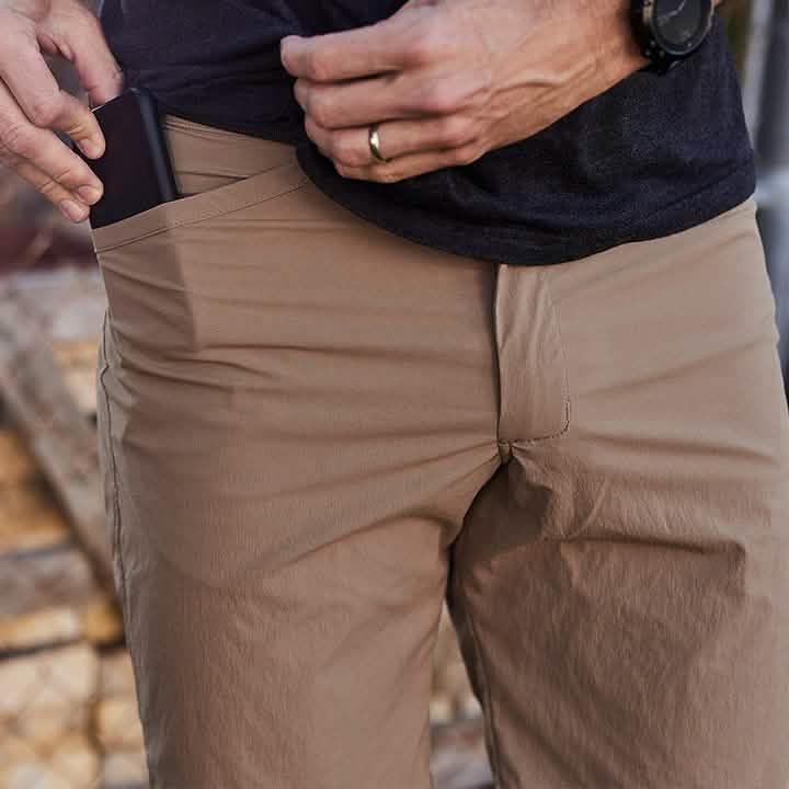 Close-up of person wearing tan GORUCK pants with hand placing phone into front pocket