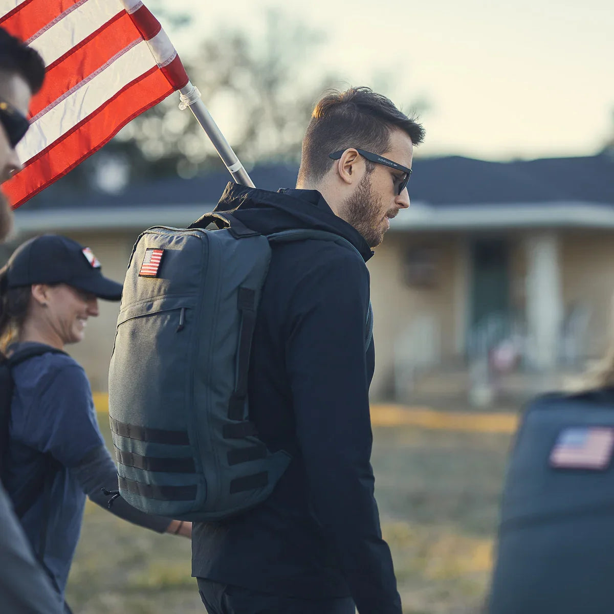 Man rucking outdoors with GORUCK backpack and American flag, group fitness event