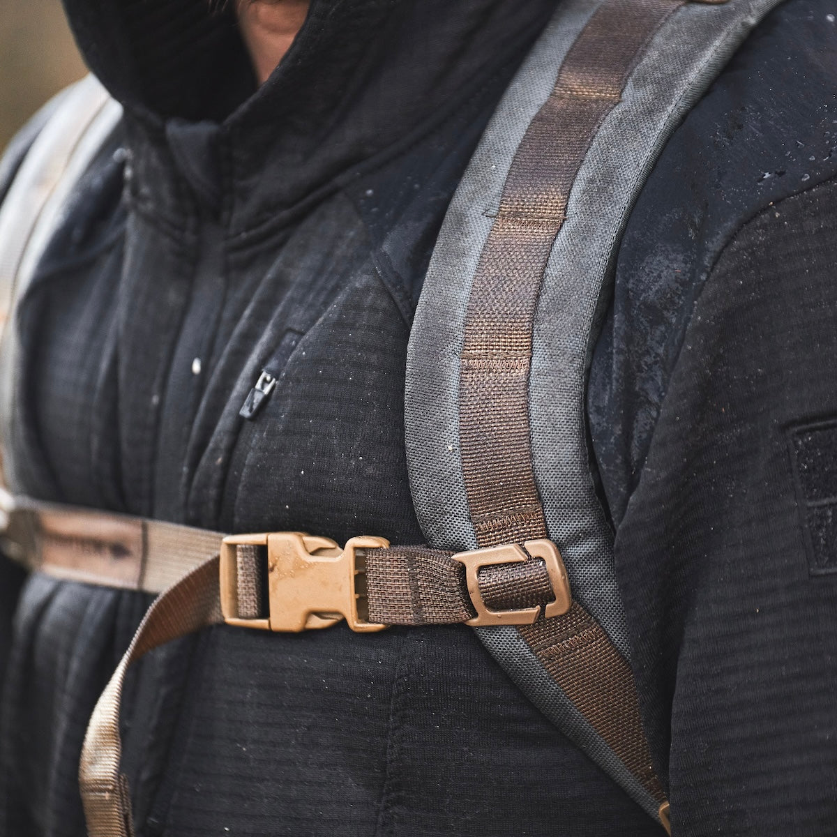 Close-up of a person wearing a black jacket and a gray backpack with brown straps and a chest buckle.