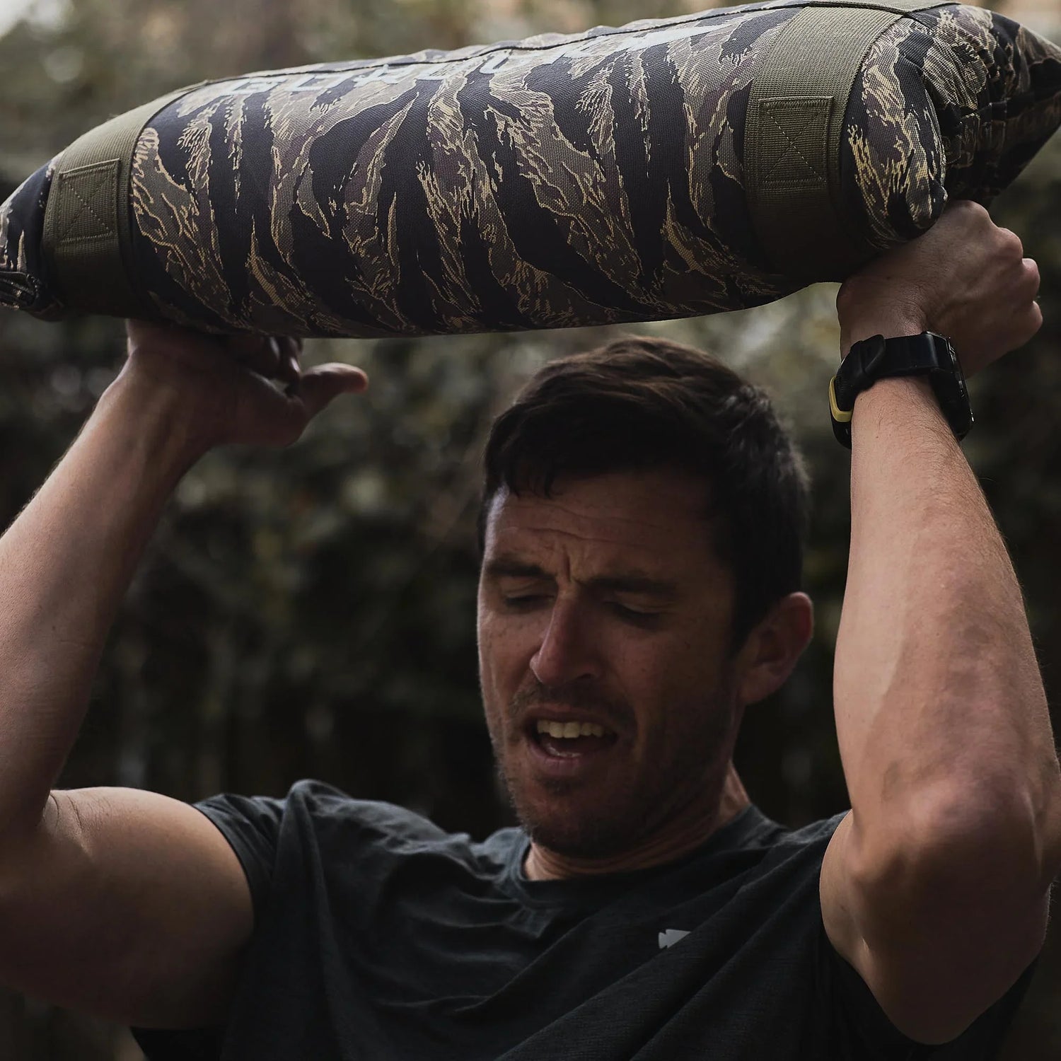 Man lifting GORUCK camo sandbag outdoors during ruck training exercise