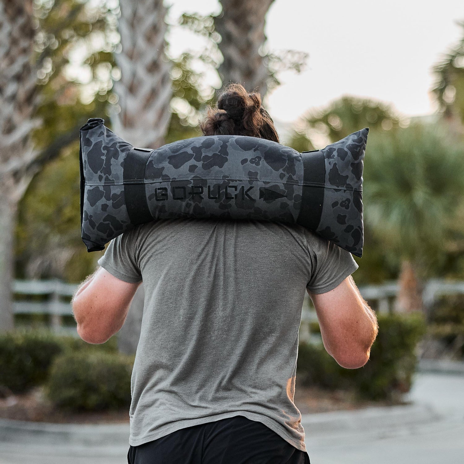 Man carrying GORUCK camo sandbag outdoors, showcasing tough rucking training gear