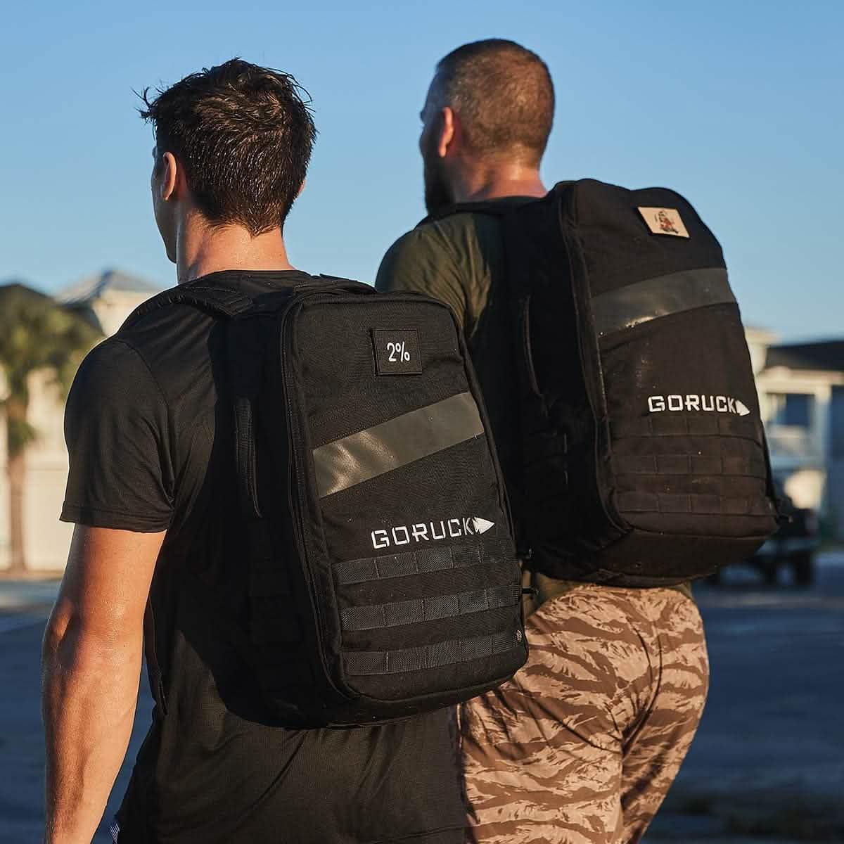 Two people outdoors wearing black GORUCK rucksacks, highlighting rugged rucking gear.