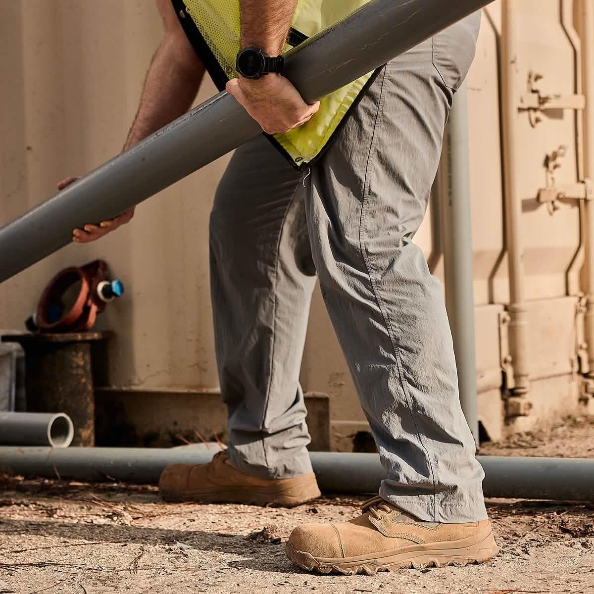Man in GORUCK tactical gear lifting pipe outdoors, wearing rugged pants and work boots