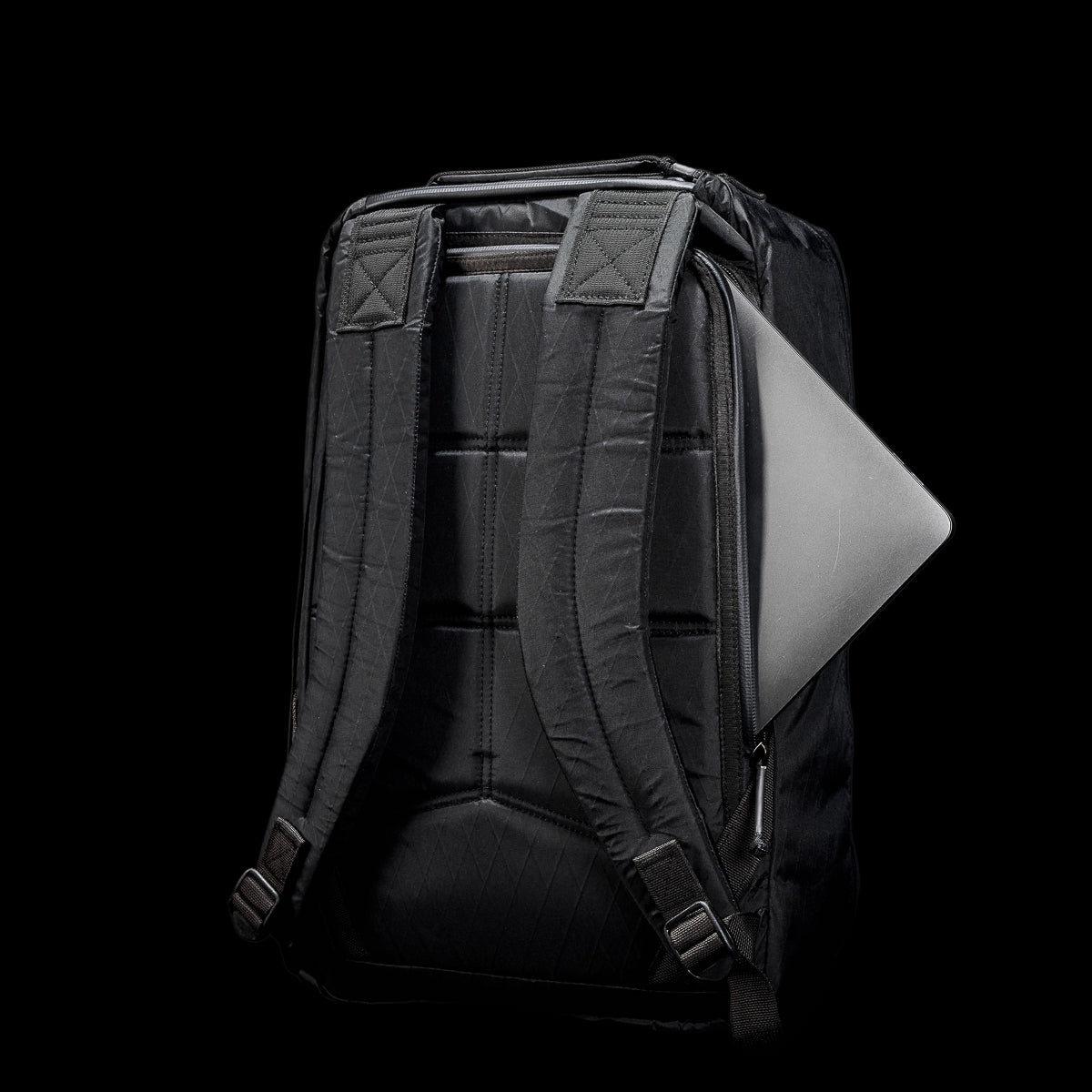 The GR1 USA - X-PAC rucksack showcases a sleek black design with a laptop partially visible in the back pocket, set against a black background, blending durability with style.