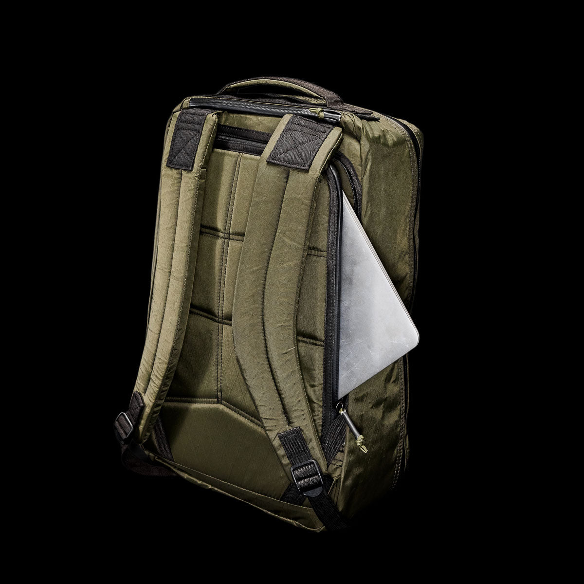 The GR1 USA - X-PAC is a green backpack with AquaGuard zippers, padded straps, and a side compartment partially showing a silver laptop. Made from durable X-PAC fabric, it stands out against the black background.