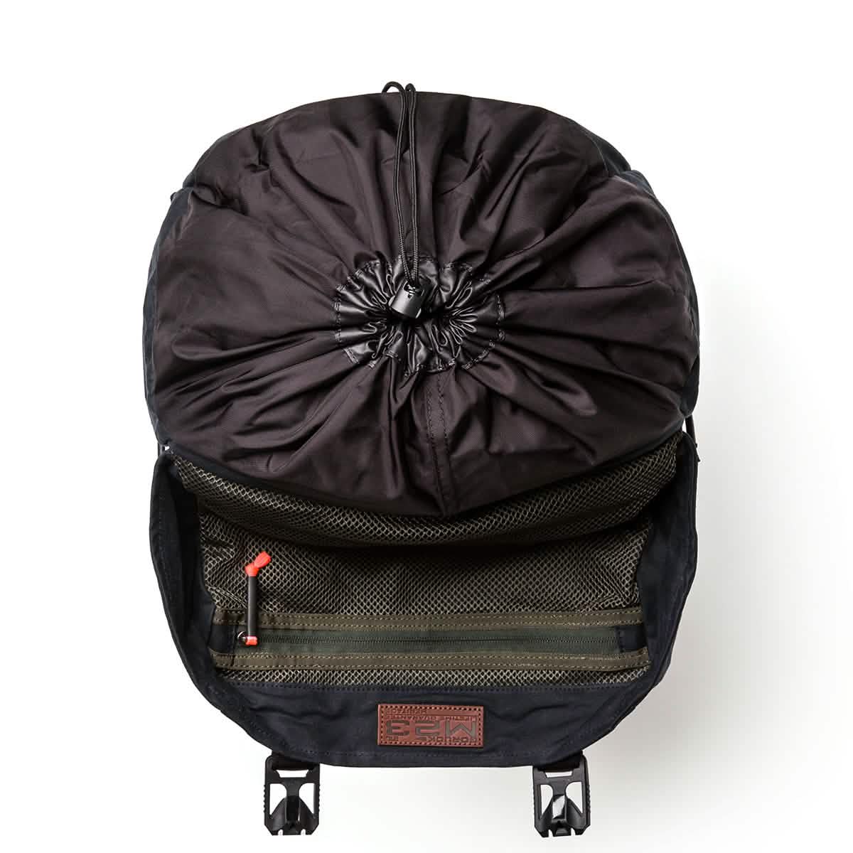 A black GORUCK M23 - Waxed Canvas rucksack featuring an open design with a drawstring closure and two interior mesh pockets. Its inner lining is visible, showcasing clips at the base and includes a bombproof laptop compartment.