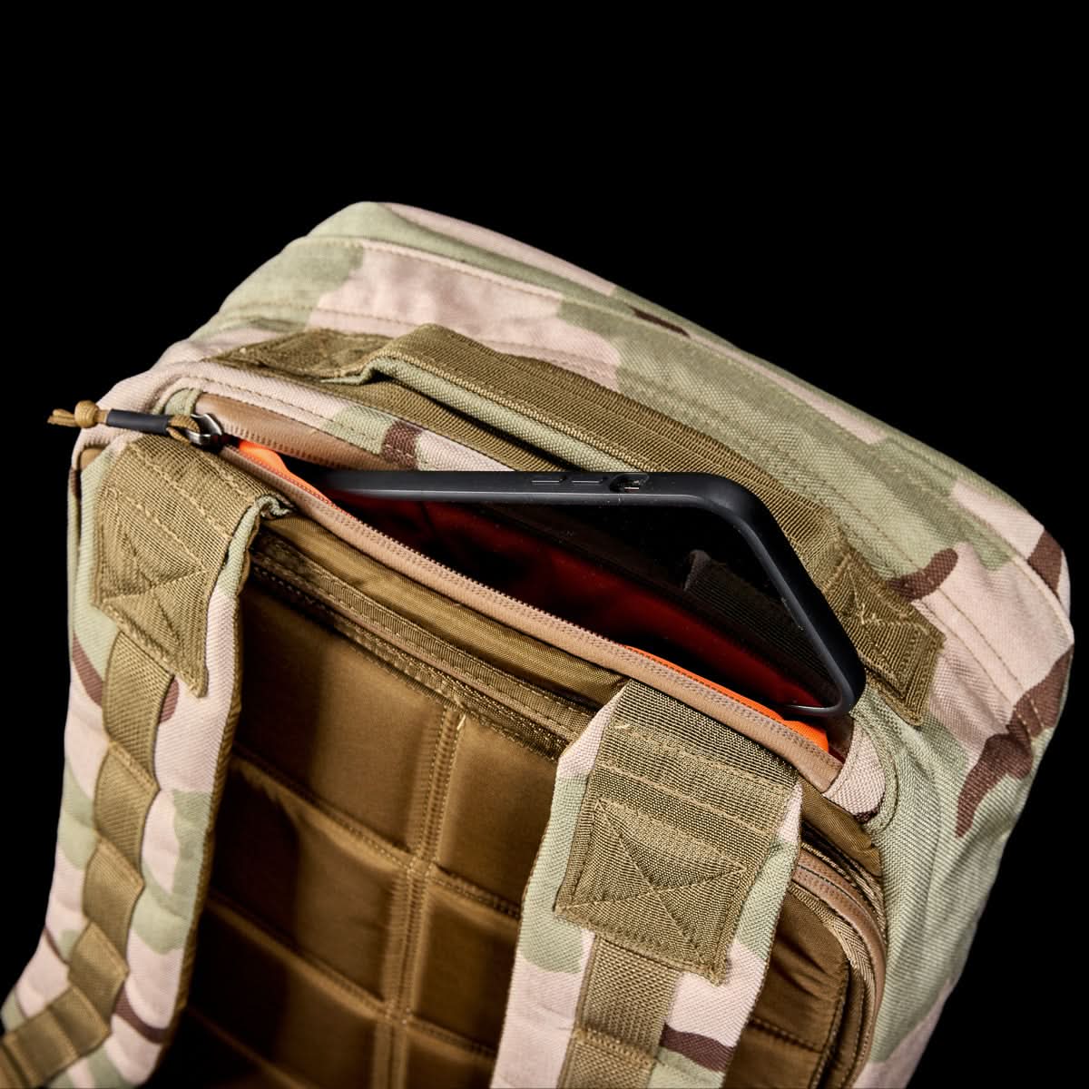 The GR1 USA - Ballistic Nylon Cordura (The Original Ruck) 210D Back Panel in camouflage shows a phone partly visible in its open front pocket, set against a black background—a rugged rucksack inspired by Special Forces.