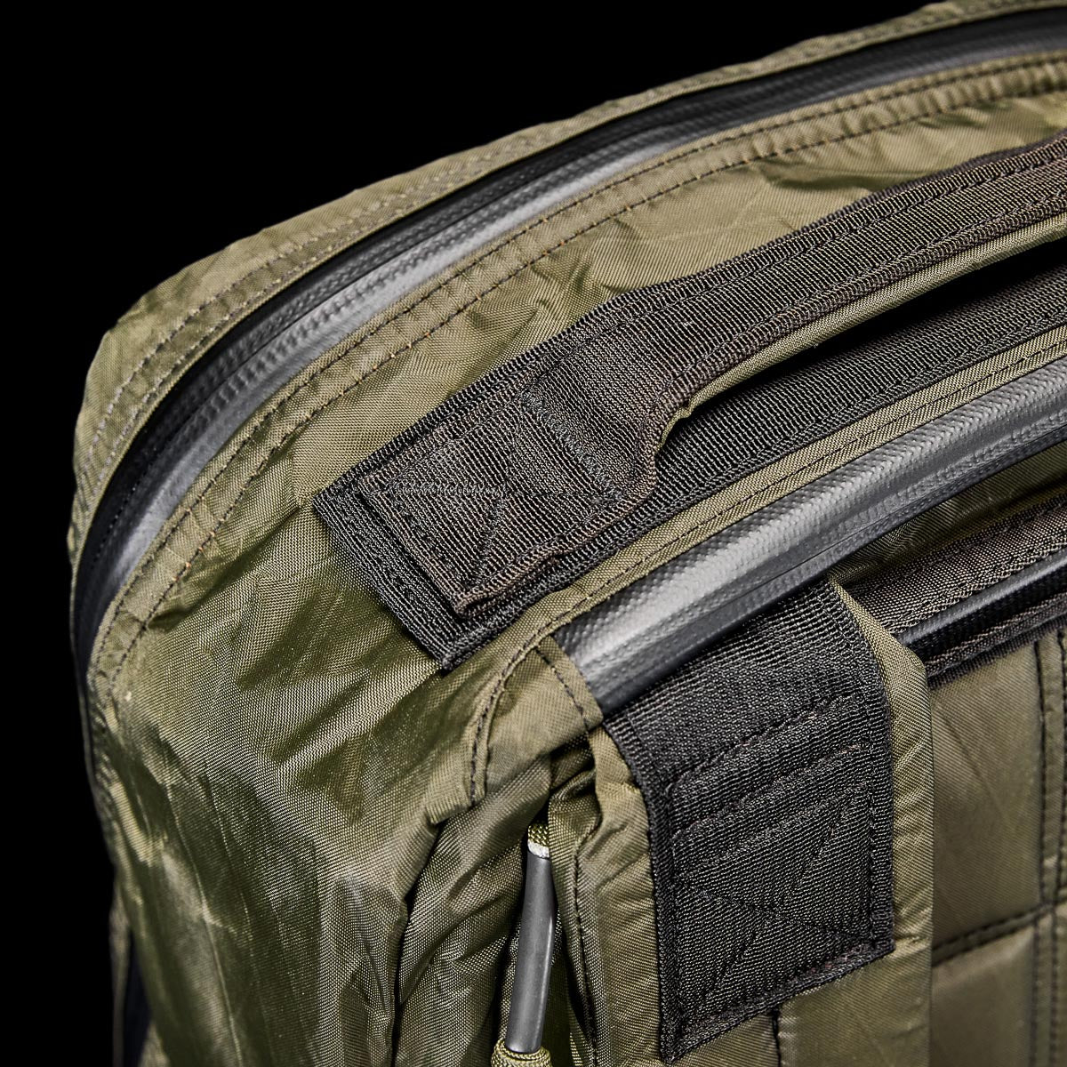 Close-up of the GR1 USA - X-PAC rucksack in green quilted fabric with black straps and zippers, set against a black background.