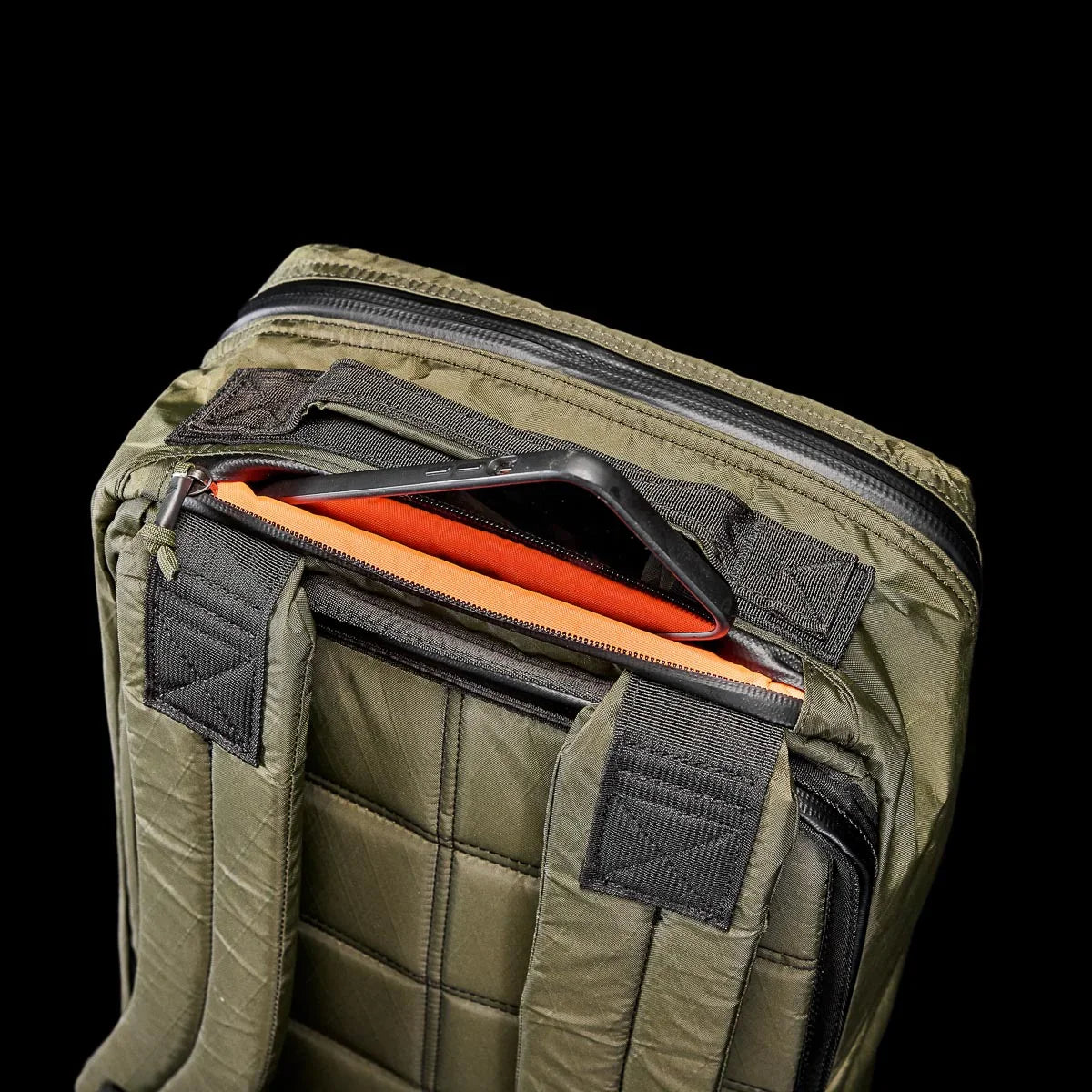 GORUCK dark green tactical backpack with padded straps and partially open top zipper showing orange interior and phone