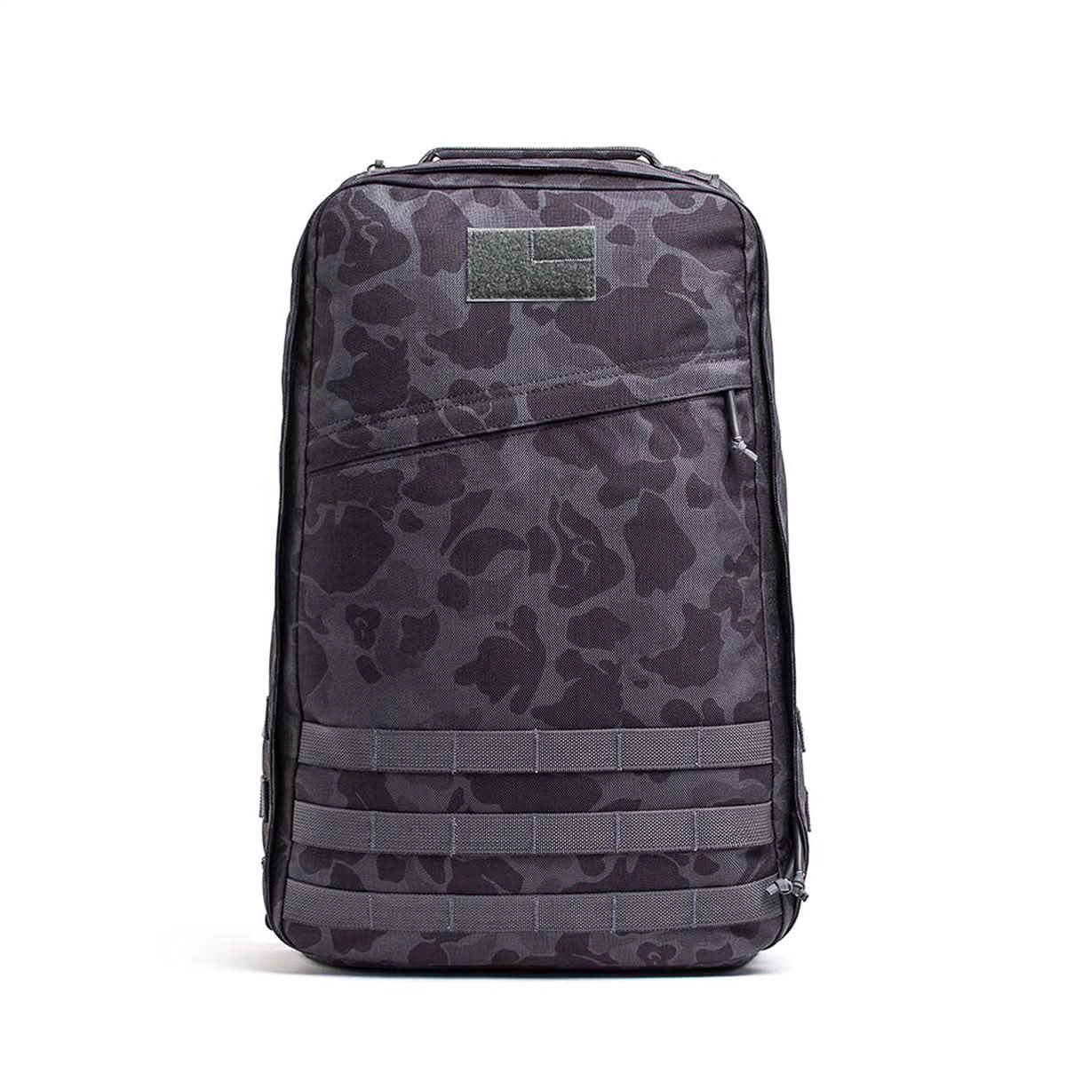 The GR1 USA - Cordura backpack features a black camo design, front zipper pocket, and horizontal straps, displayed against a white background.