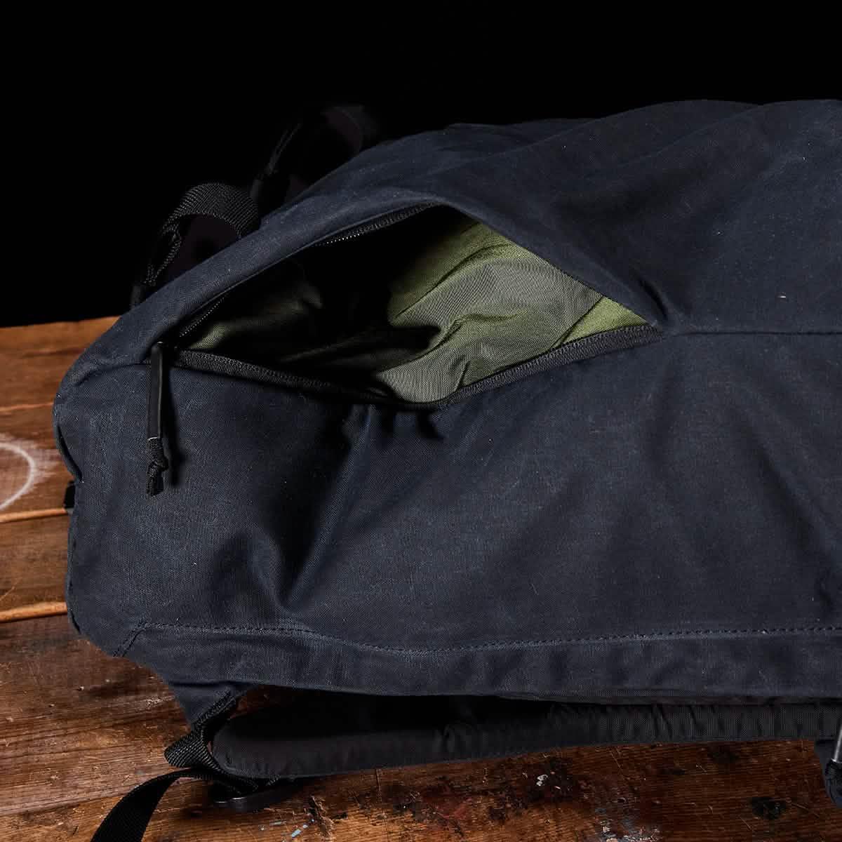 Black GORUCK backpack made from rugged material on wooden surface with an open zipper showing green fabric inside