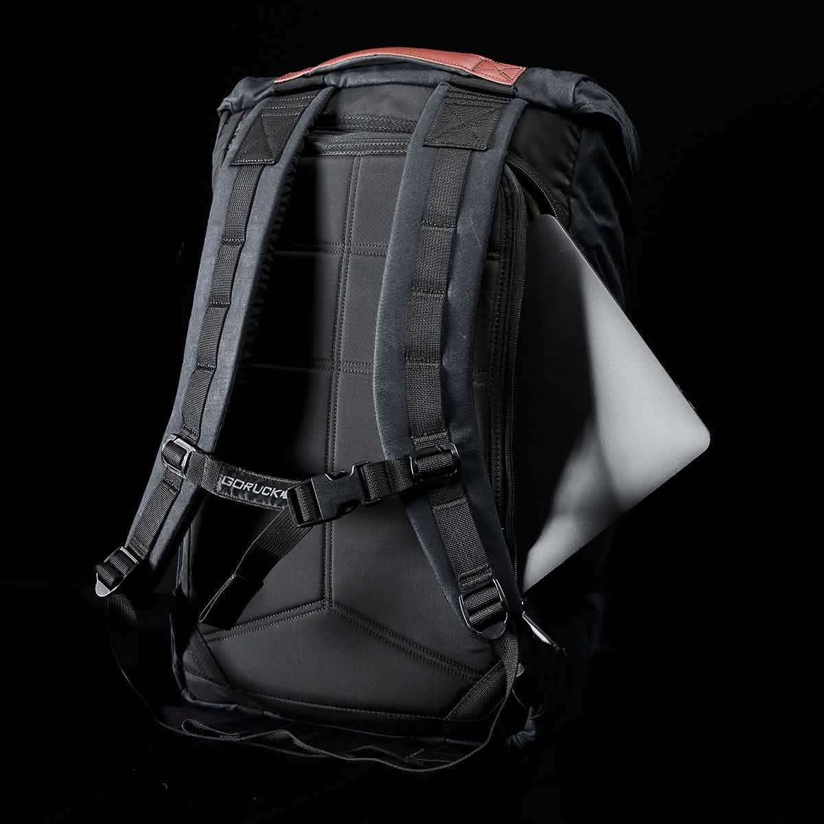 GORUCK black tactical backpack with padded straps and laptop partially inserted in side pocket against black background