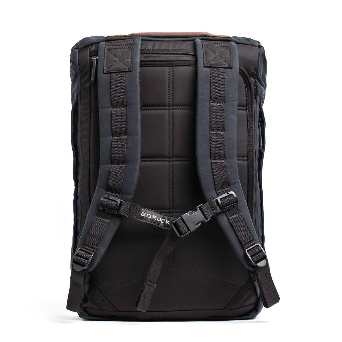 The GORUCK M23 - Waxed Canvas rucksack is displayed from the back, crafted from robust materials. It includes padded shoulder straps and a chest strap, showcasing a military-inspired yet sleek, minimalist appearance with visible stitching and a label on the strap.