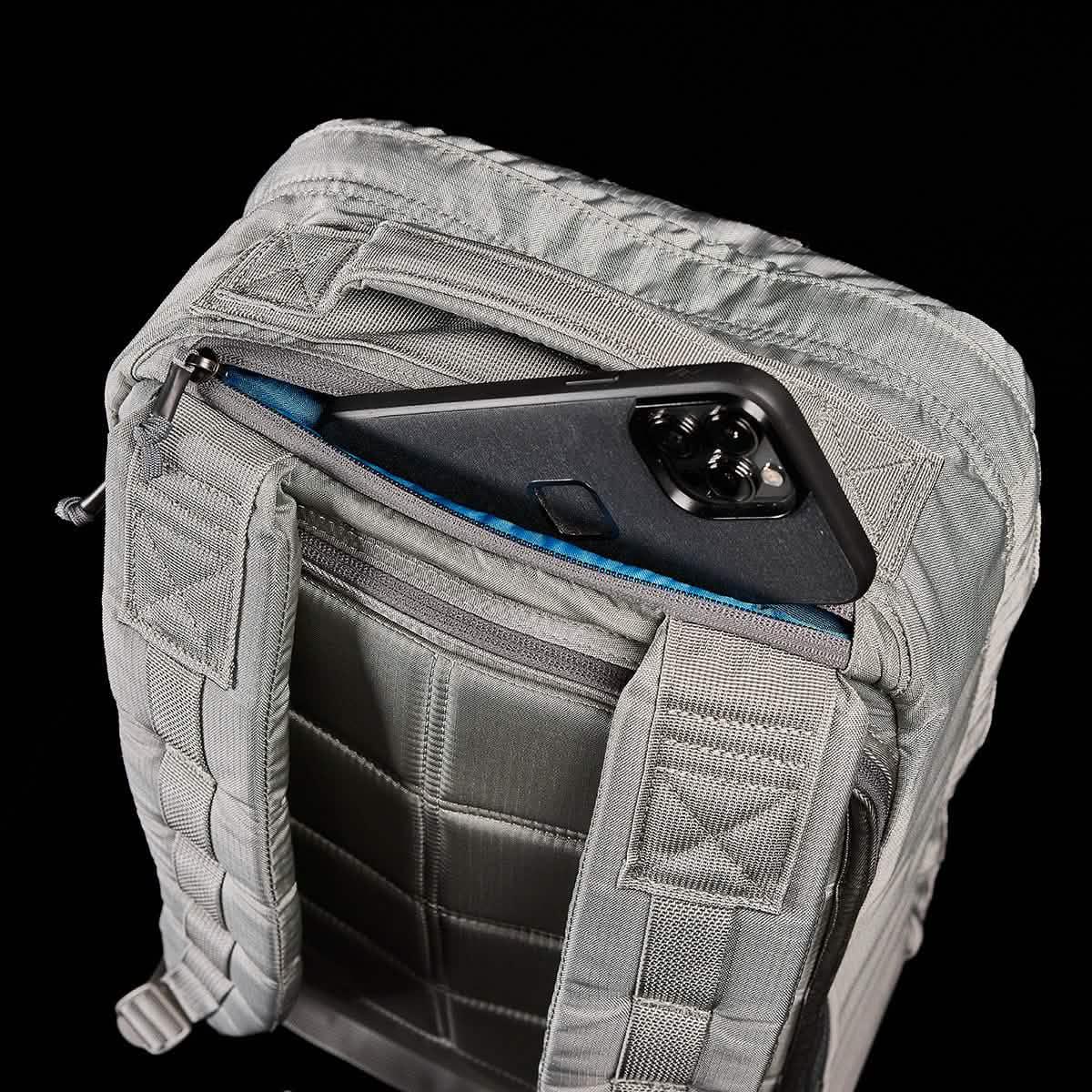 Close-up of gray tactical backpack back panel with padded straps and a smartphone partially tucked into a zippered pocket