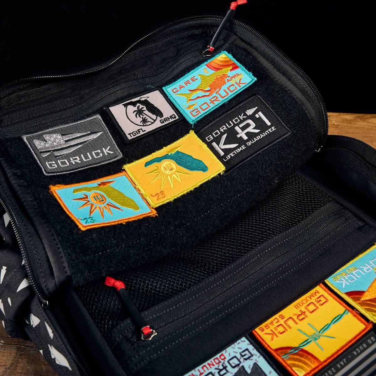 Open school backpack revealing the REFLECTIVE KR1, colorful rectangular embroidered patches attached to its black inner panel.