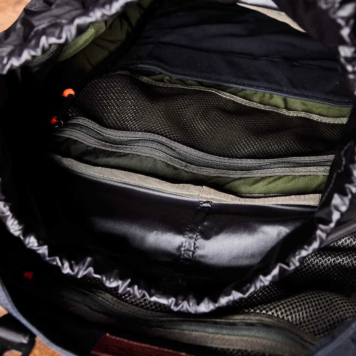 An open view of the M23 - Waxed Canvas reveals its modern design, featuring multiple zippered compartments. The interior is lined with dark fabric and mesh pockets, accented by orange zipper pulls for organized storage that reflects the GORUCK standard.