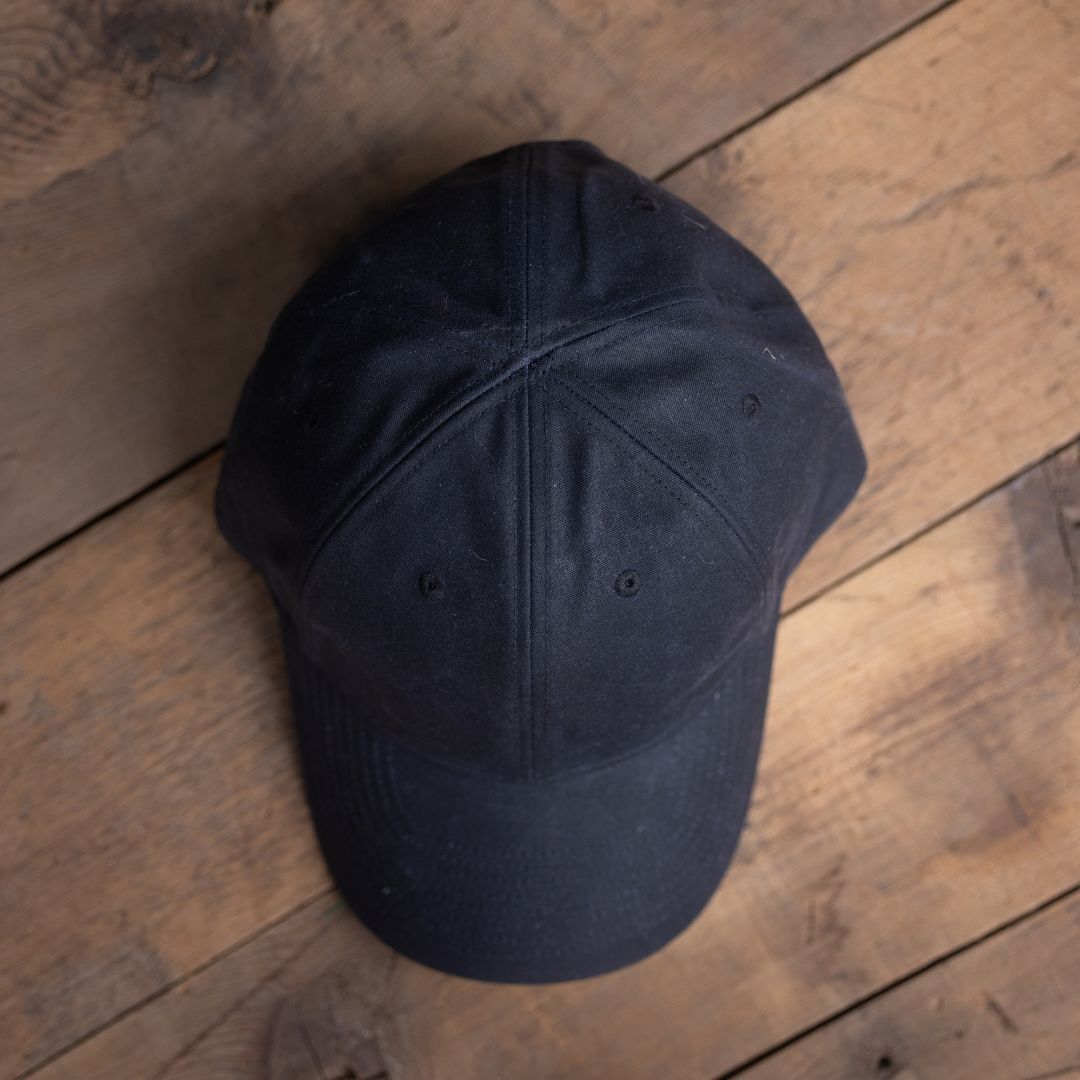 The Tac Hat - Heritage, a black baseball cap, displayed on a wooden surface and viewed from above.