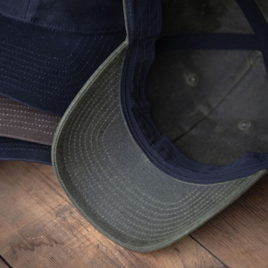 Close-up of two Tac Hat - Heritage caps overlapping on a wooden surface, highlighting the brims and intricate stitching details.