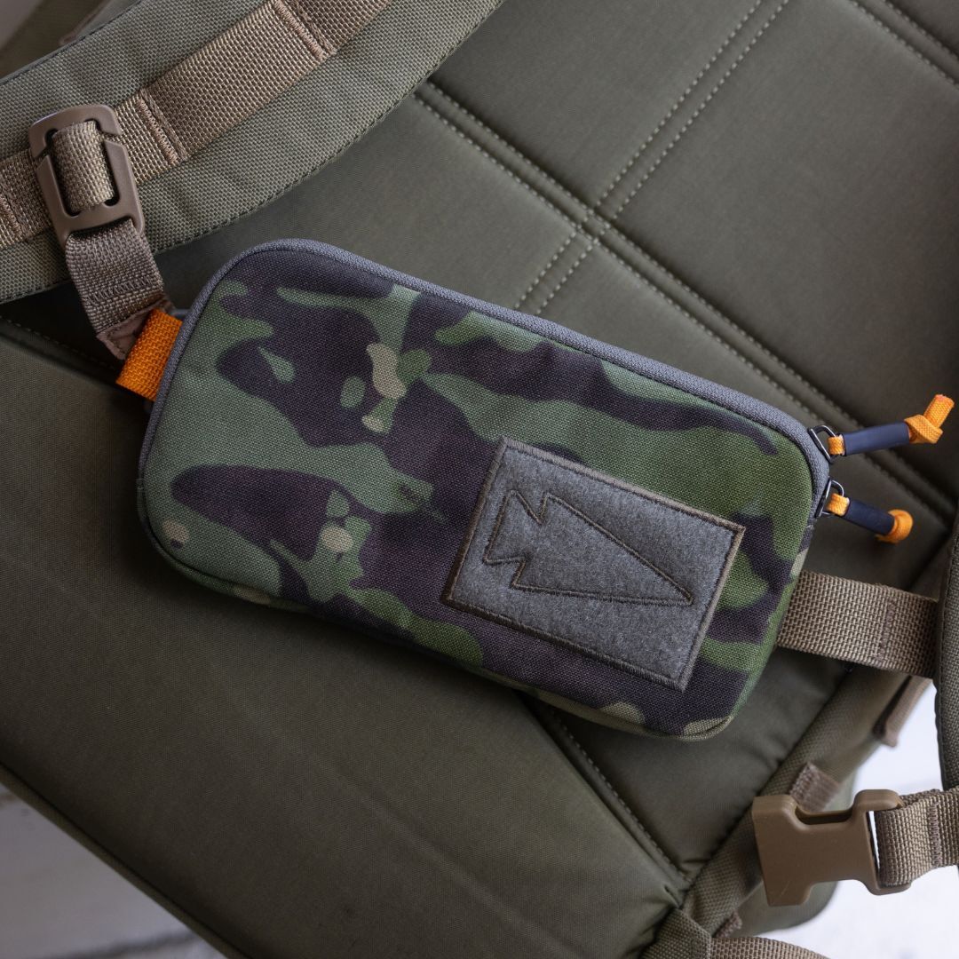 Sternum / Belt Pouch - CORDURA in camouflage, featuring a patch and two zipper pulls, attached to a strap on a green padded surface for hands-free convenience during rucking.