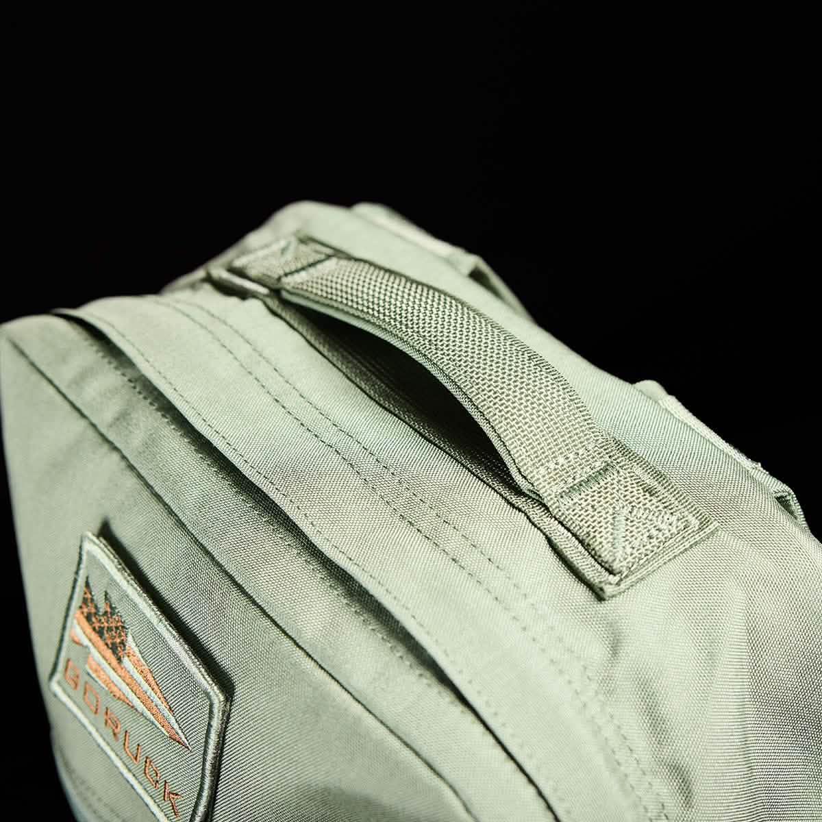 Close-up of durable olive green GORUCK rucksack handle with stitched logo patch on black background