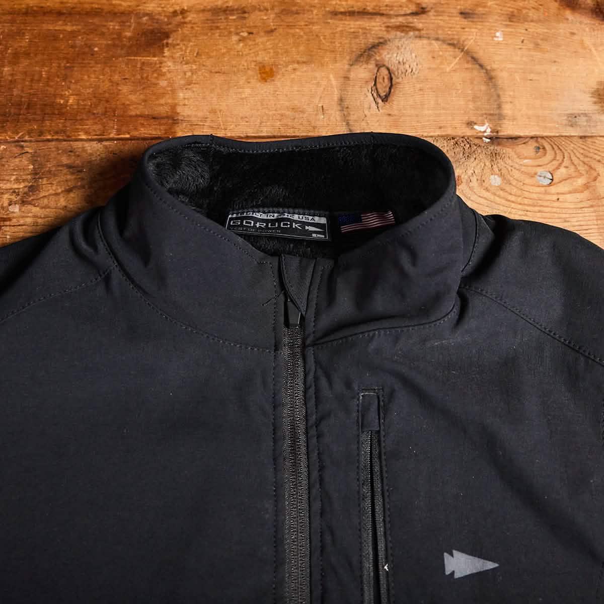 Close-up of black GORUCK jacket with zippered chest pocket and fleece-lined collar on wooden surface