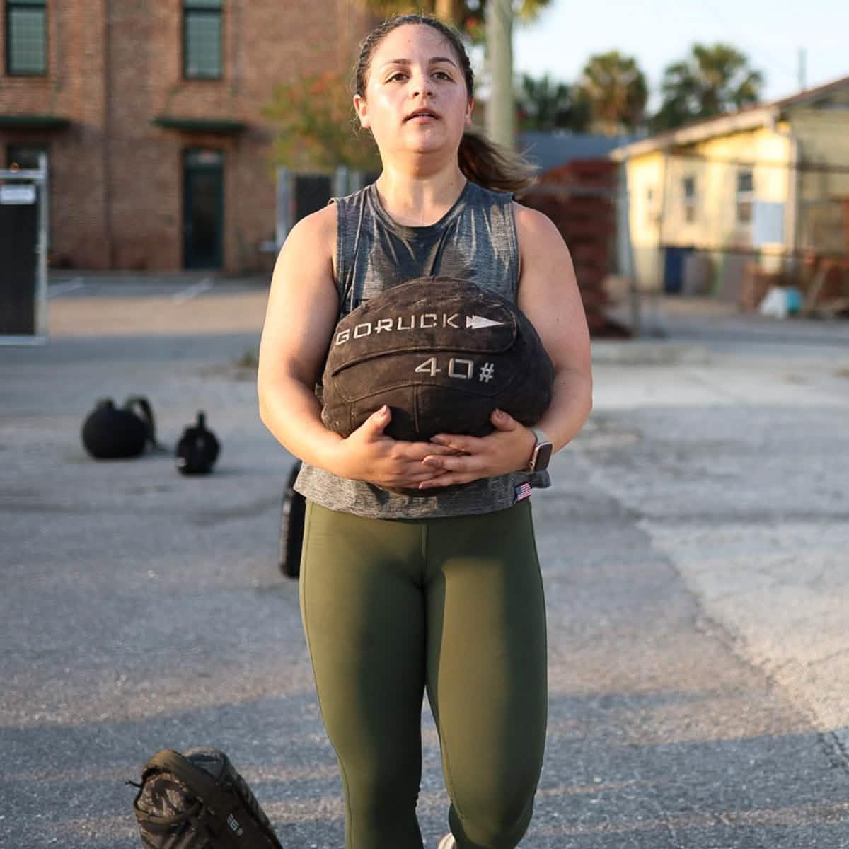 Woman exercising outdoors holding a GORUCK 40-pound weighted sandbag during fitness training