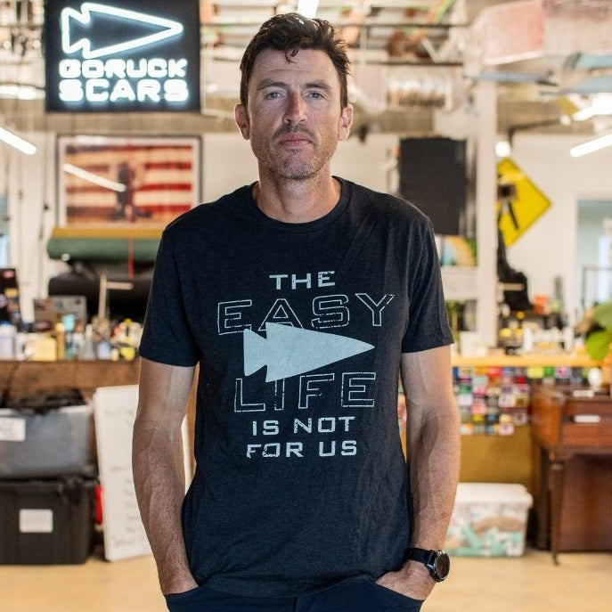 A man is standing in a workshop, wearing the “Easy Life Is Not For Us” black shirt.