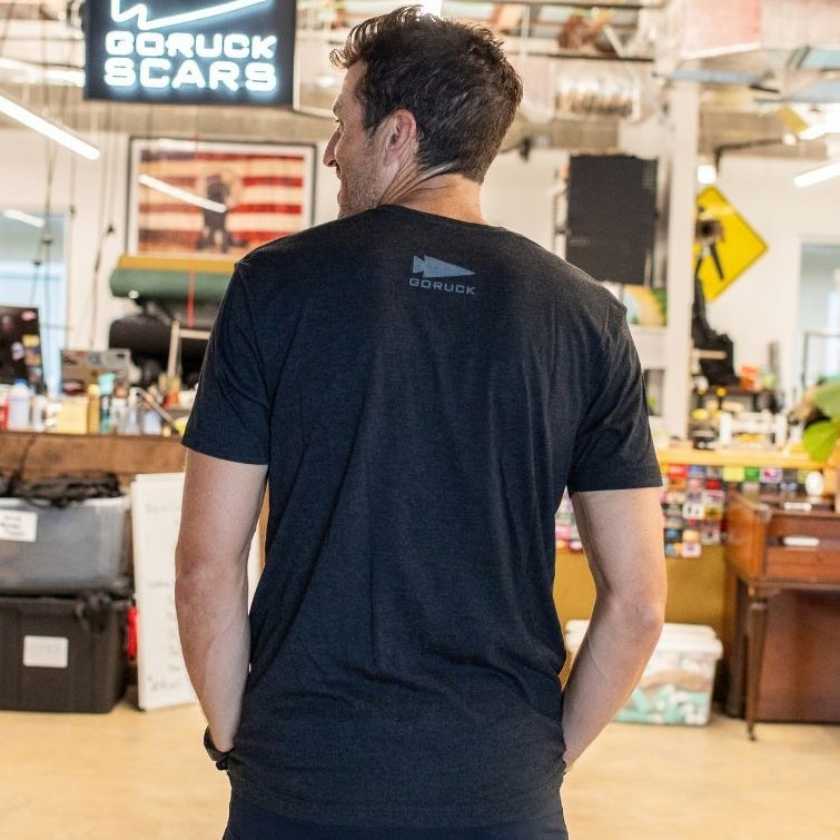 A man stands in an office, facing away, with a “DFQ” sign visible in the background.