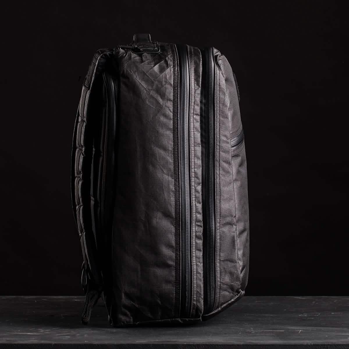 The GR2 USA x Carryology - Ultra Black backpack, made from Challenge Sailcloth UHMWPE, stands upright with visible zippers against a dark background.