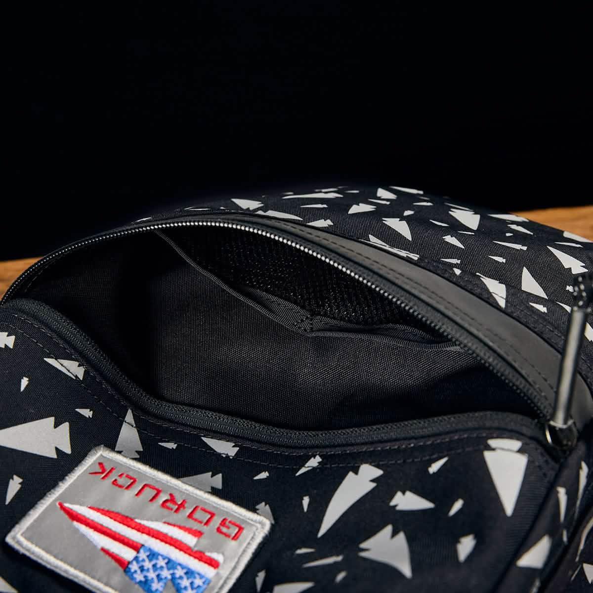Opened REFLECTIVE KR1 kids rucksack in black with white geometric patterns, zippered pocket, and American flag patch—a durable, reflective book bag ideal for school.