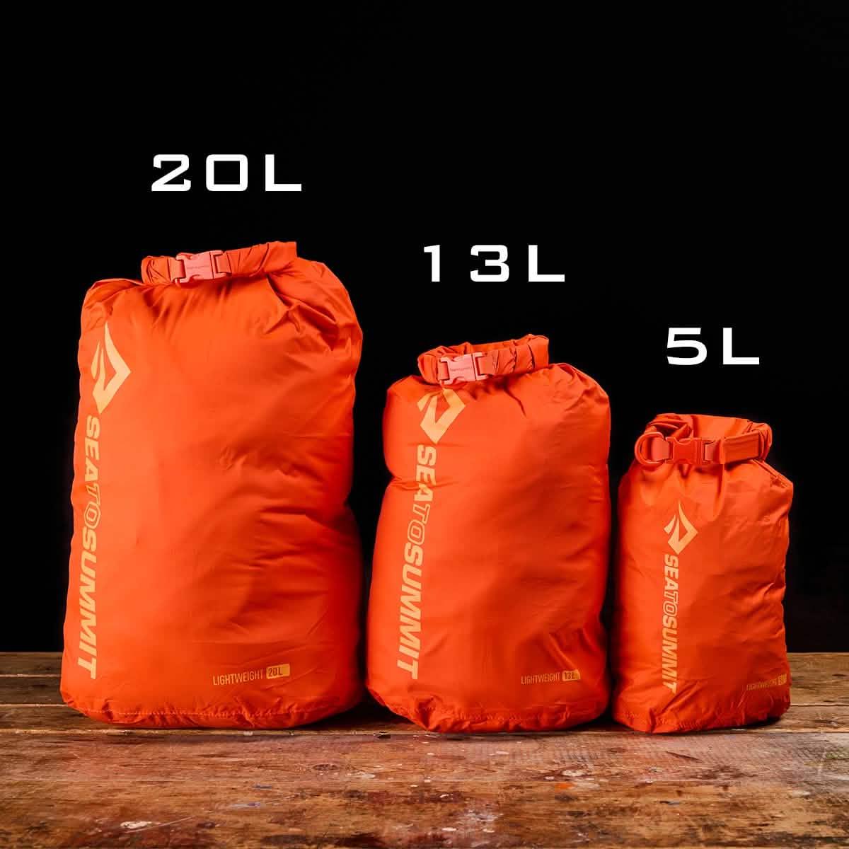 Three bright orange Sea to Summit lightweight dry bags in 20L, 13L, and 5L sizes on wooden surface