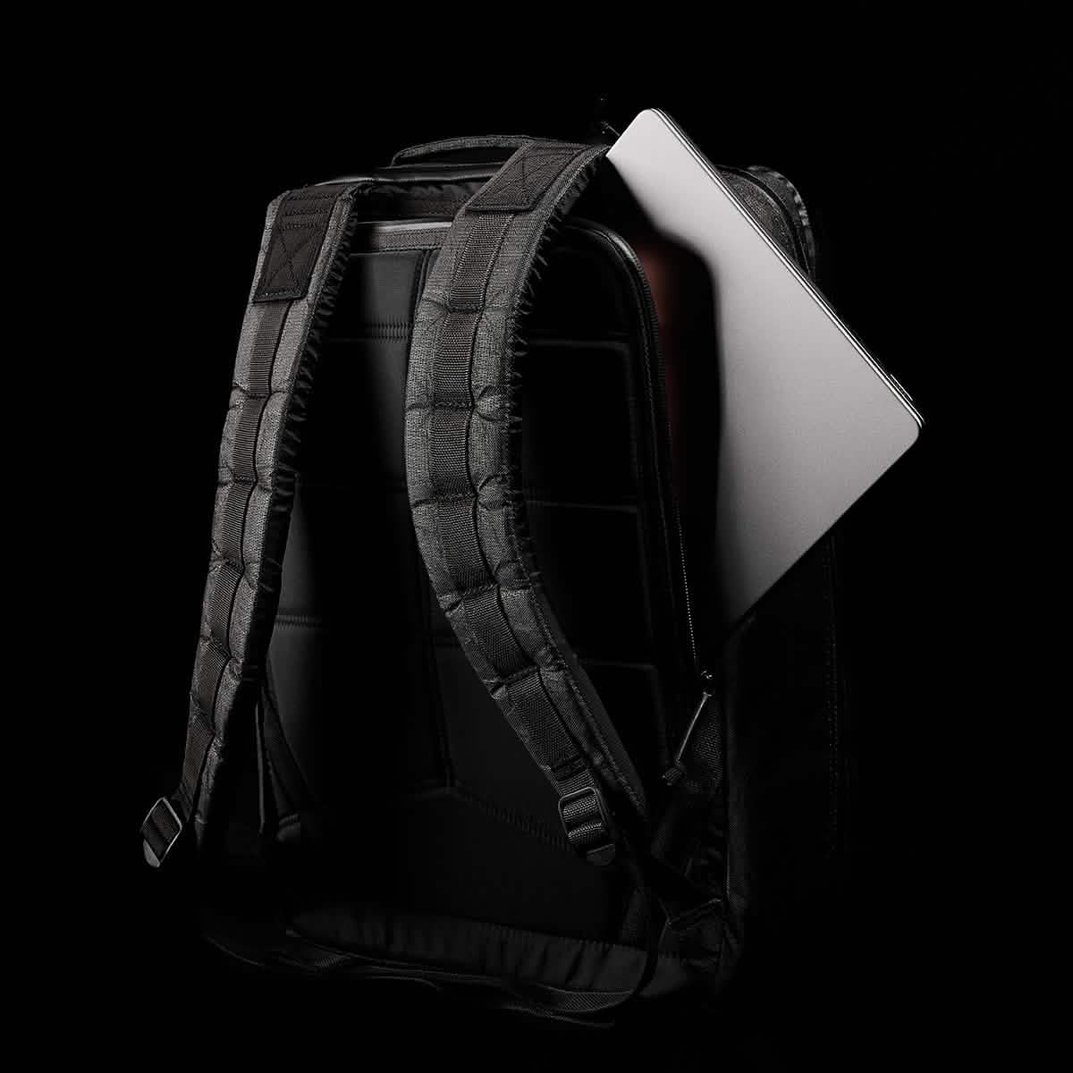 A GR2 USA x Carryology - Ultra Black backpack, crafted from tough UHMWPE fabric, with a gray laptop partially visible inside, set against a black background.