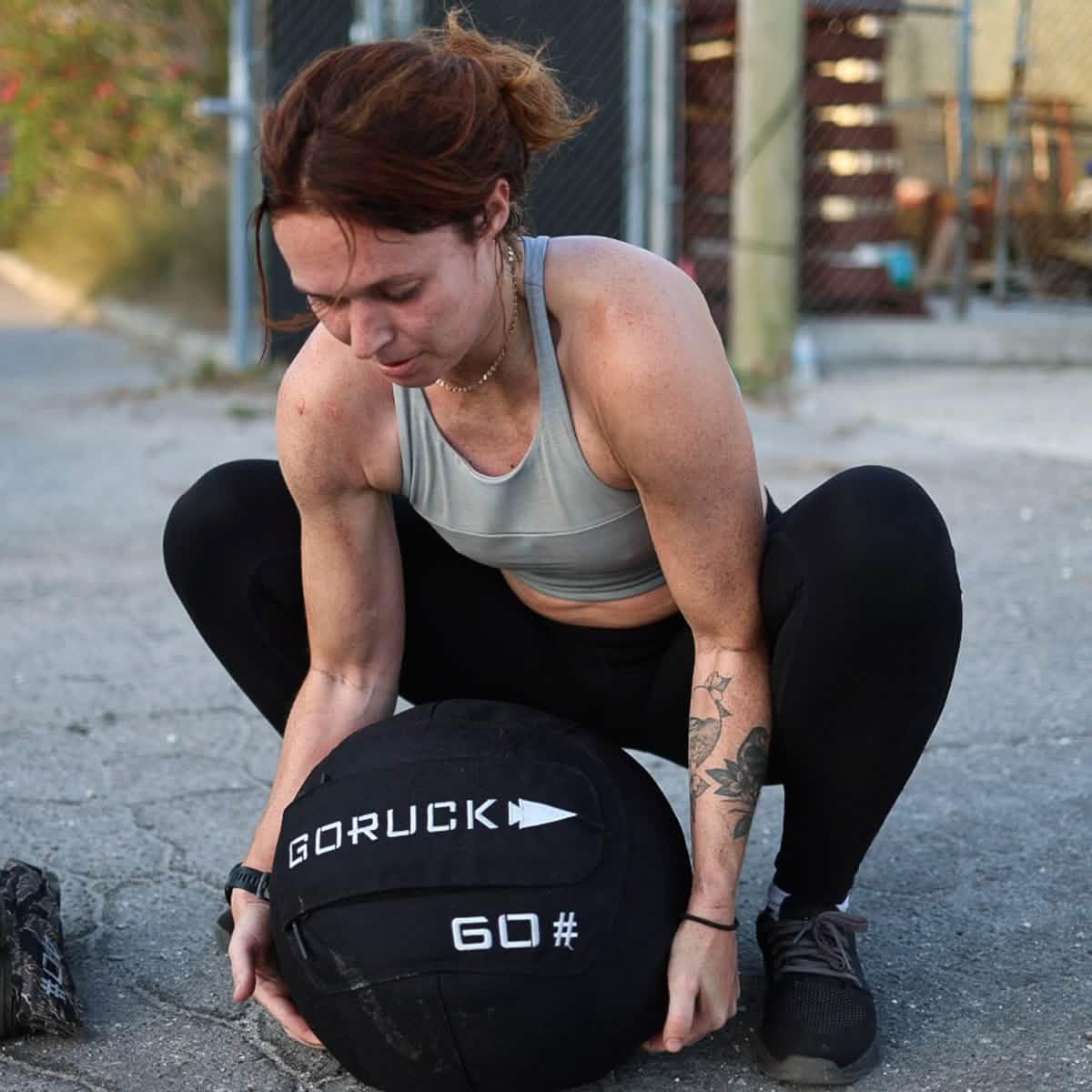 Athletic woman lifting GORUCK 60-pound weighted ruck sack outdoors on pavement