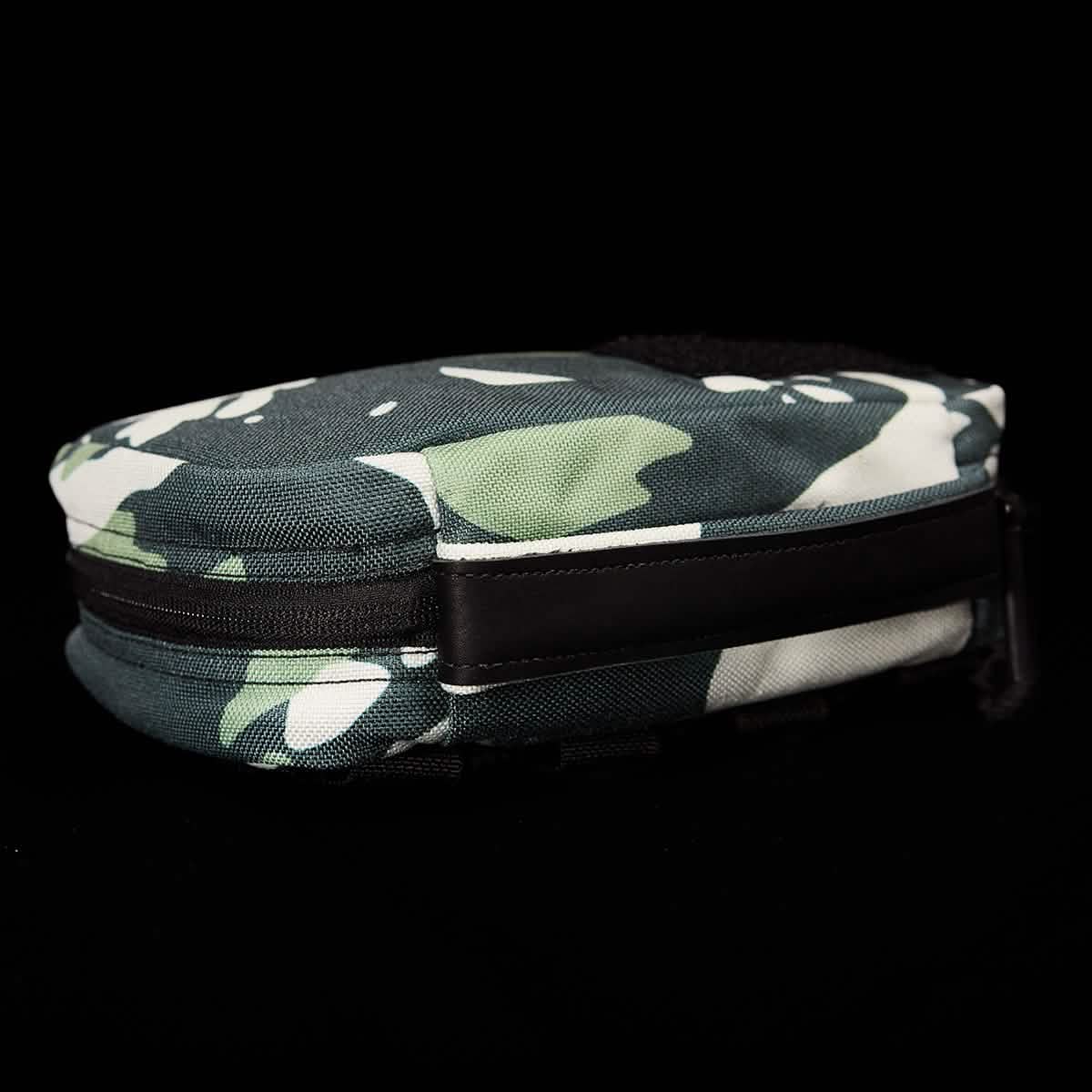 Against a black backdrop lies the GR1 Field Pocket x Gear Patrol by GORUCK, a compact, zippered pouch adorned with a green, black, and white Variegated Elephant Ear Camo pattern.